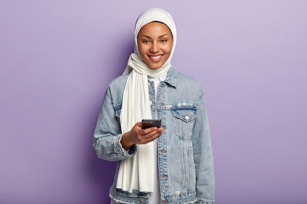 Retrato de mujer musulmana joven feliz posando con su teléfono