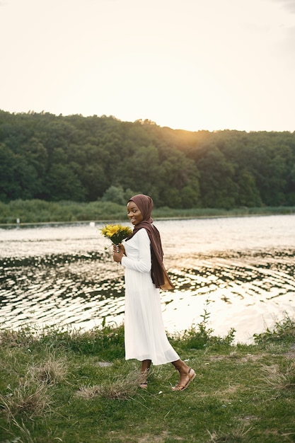Retrato de una mujer musulmana de pie cerca del río sosteniendo un ramo de flores