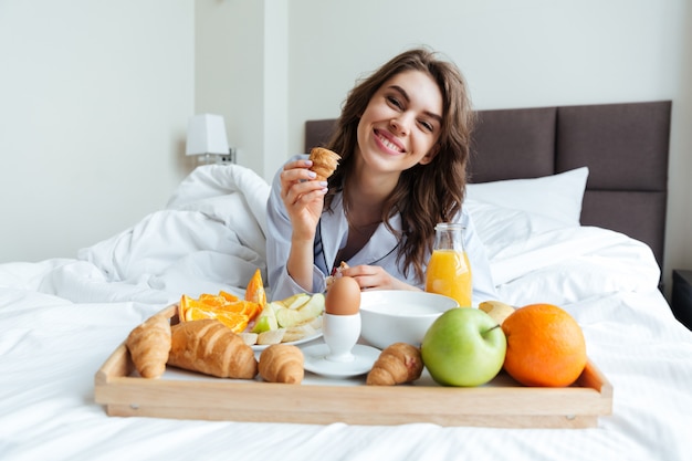 Retrato de una mujer muy feliz desayunando en la cama