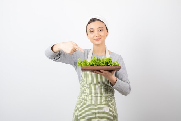 Retrato de una mujer muy linda apuntando a una tabla de madera con lechuga fresca