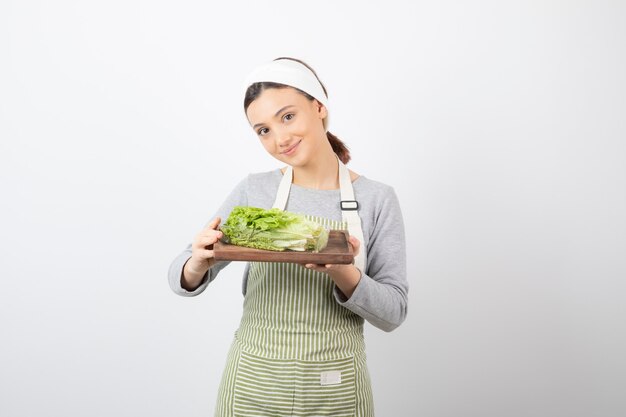 Retrato de una mujer muy linda sosteniendo una tabla de madera con lechuga fresca