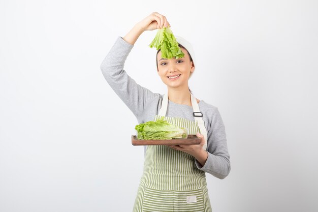 Retrato de una mujer muy linda sosteniendo una tabla de madera con lechuga fresca