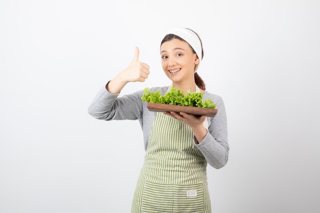 Retrato de una mujer muy linda con una tabla de madera de lechuga fresca mostrando un pulgar hacia arriba