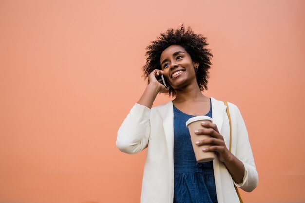 Retrato de mujer de negocios afro hablando por teléfono mientras está de pie al aire libre en la calle. Concepto urbano y empresarial.