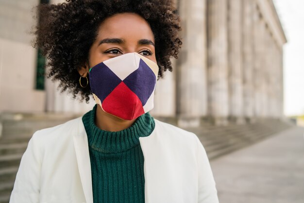 Retrato de mujer de negocios afro con máscara protectora mientras está de pie al aire libre en la calle. Concepto urbano y empresarial.