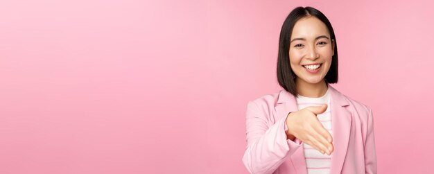 Retrato de una mujer de negocios agradable y sonriente estrechando la mano con un apretón de manos de un socio comercial extendiendo la mano y saludando de pie sobre un fondo rosa