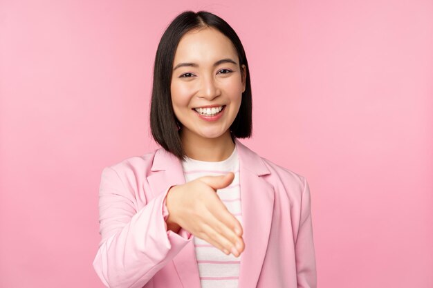 Retrato de una mujer de negocios agradable y sonriente estrechando la mano con un apretón de manos de un socio comercial extendiendo la mano y saludando de pie sobre un fondo rosa