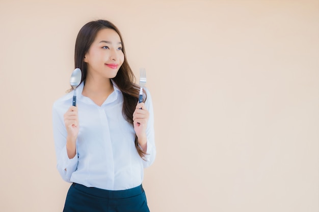 Retrato de mujer de negocios asiática joven hermosa con cuchara y tenedor listo para comer