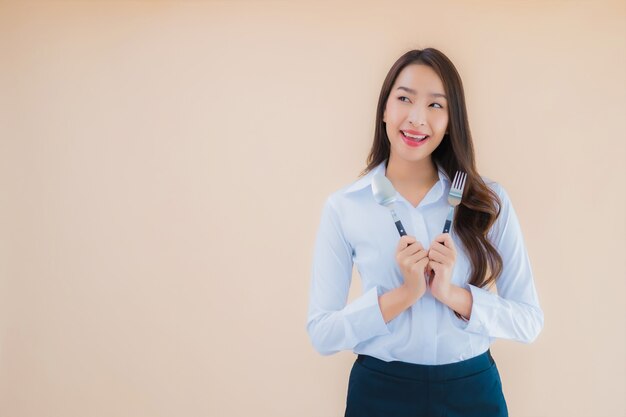 Retrato de mujer de negocios asiática joven hermosa con cuchara y tenedor listo para comer