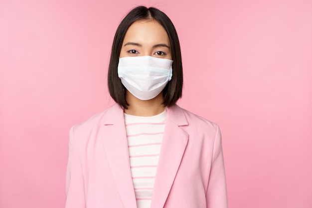 Retrato de una mujer de negocios asiática con mascarilla médica usando traje concepto de trabajo de oficina durante la pandemia de covid19 de pie sobre fondo rosa