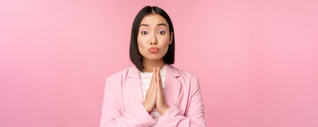 Retrato de una mujer de negocios asiática que pide ayuda, diga por favor pararse en oración suplicando pose rosa stu