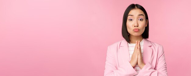 Retrato de una mujer de negocios asiática que pide ayuda, diga por favor, de pie en rezar, rogar, posar, fondo de estudio rosa