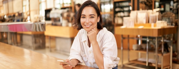 Foto gratuita retrato de una mujer de negocios asiática sentada en una mesa en un café bebiendo café leyendo en una aplicación para teléfonos inteligentes