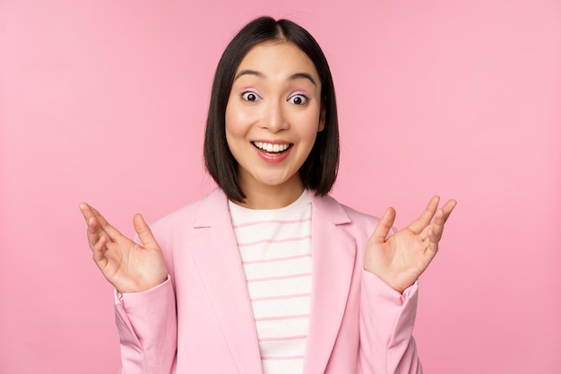 Retrato de una mujer de negocios asiática sorprendida por la cámara aplaudiendo y mirando emocionada sonriendo posando contra un fondo rosa