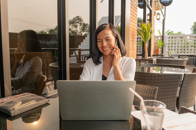 Retrato de mujer de negocios en un café usando una computadora portátil y hablando con teléfono celular