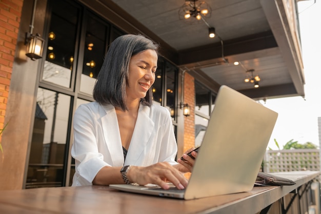 Retrato de mujer de negocios en un café usando una computadora portátil y un teléfono móvil