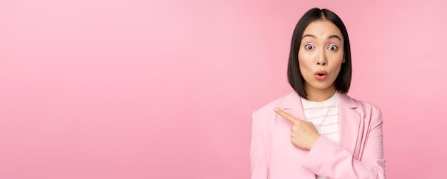 Retrato de mujer de negocios con cara sorprendida señalando con el dedo a la izquierda mostrando algo interesante de pie