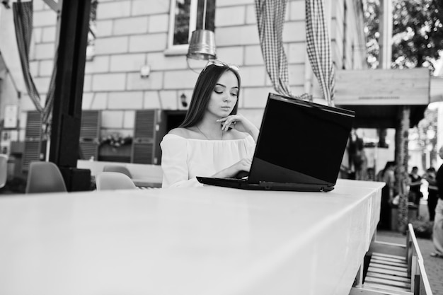 Retrato de una mujer de negocios exitosa e independiente fuerte que usa ropa informal inteligente y gafas que trabajan en una computadora portátil en un café Foto en blanco y negro