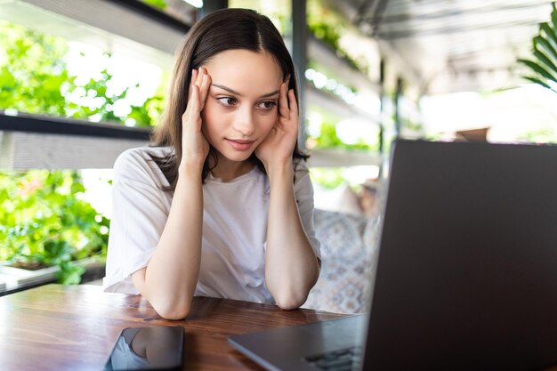 Retrato de mujer de negocios joven cansada con ordenador portátil. Empresaria cansada que tiene dolor de cabeza mientras trabaja en su computadora portátil en la cafetería.