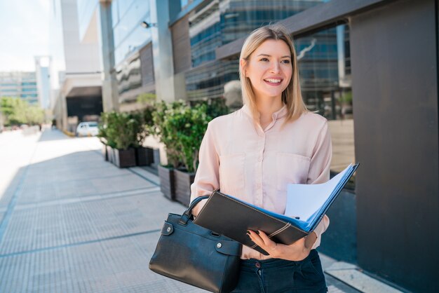 Retrato de mujer de negocios joven sosteniendo el portapapeles mientras está parado al aire libre en la calle. Concepto de negocio.