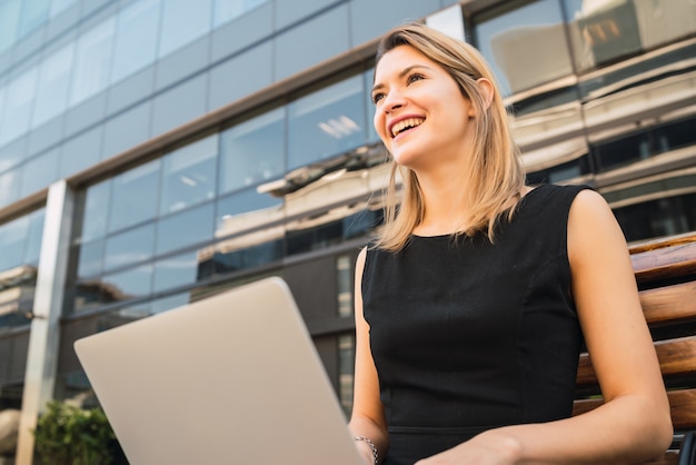 Retrato de mujer de negocios joven usando su computadora portátil mientras está sentado al aire libre en la calle. Concepto de negocio.