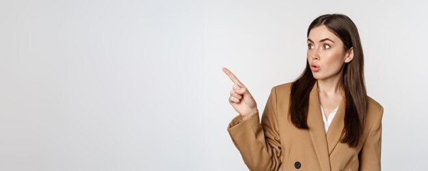 Retrato de una mujer de negocios que señala con el dedo a la izquierda mostrando el logotipo de la pancarta corporativa de pie con traje marrón