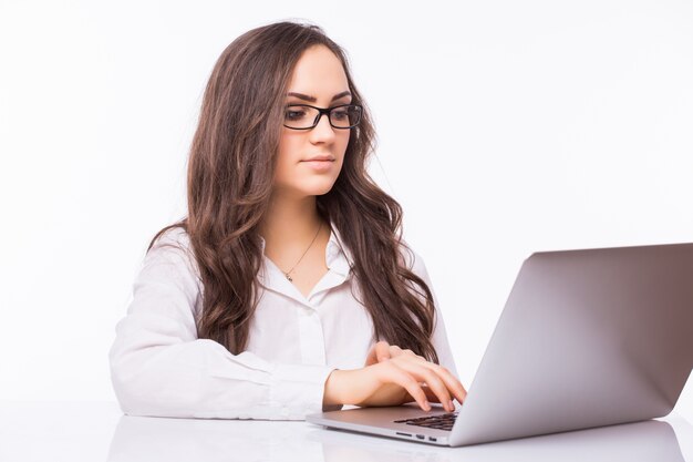 Retrato de mujer de negocios sentada en su escritorio trabajando con portátil aislado sobre pared blanca.