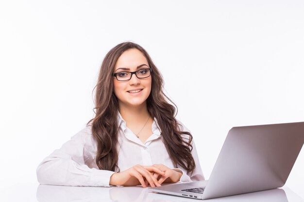 Retrato de mujer de negocios sentada en su escritorio trabajando con portátil aislado sobre pared blanca.