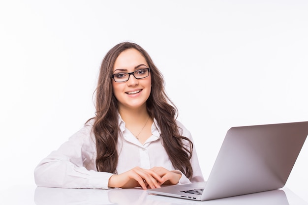 Retrato de mujer de negocios sentada en su escritorio trabajando con portátil aislado sobre pared blanca.