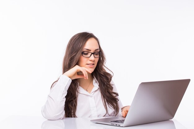 Retrato de mujer de negocios sentada en su escritorio trabajando con portátil aislado sobre pared blanca.