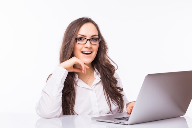 Retrato de mujer de negocios sentada en su escritorio trabajando con portátil aislado sobre pared blanca.