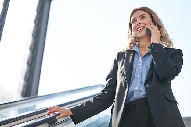 Retrato de una mujer de negocios con traje parada en una escalera mecánica caminando por la ciudad usando una empresa de telefonía móvil