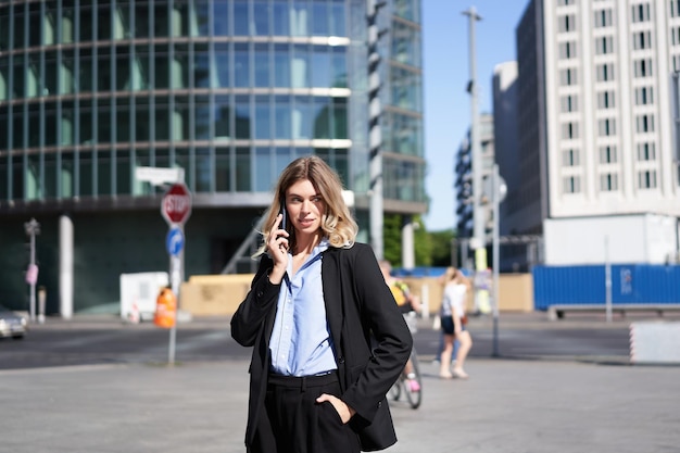 Retrato de mujer de negocios en traje de pie en la calle con teléfono móvil de guardia con alguien sonriendo