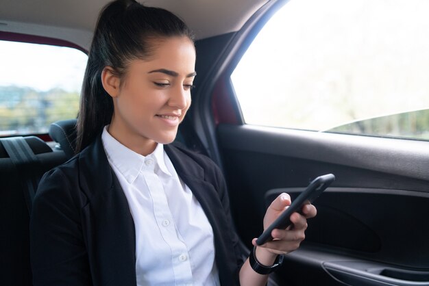 Retrato de mujer de negocios usando su teléfono móvil de camino al trabajo en un coche