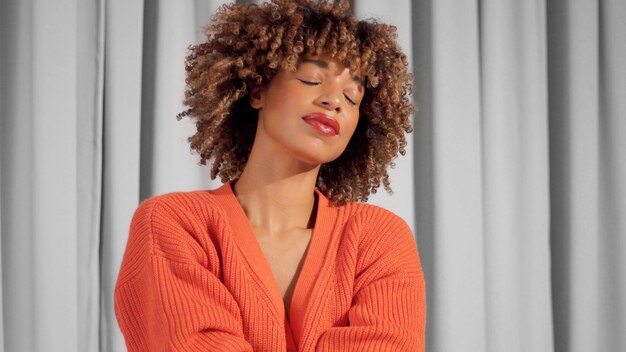 Retrato de una mujer negra de raza mixta con cabello rizado texturizado en una chaqueta naranja brillante con maquillaje natural para tonos de piel oscuros con los ojos cerrados