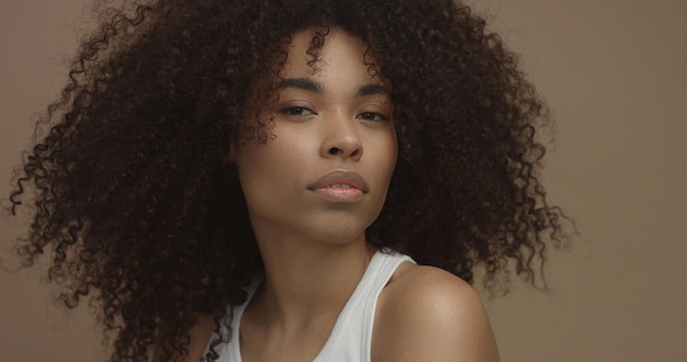 Retrato de mujer negra de raza mixta con pelo rizado de pelo afro grande en fondo beige Primer plano de la cara