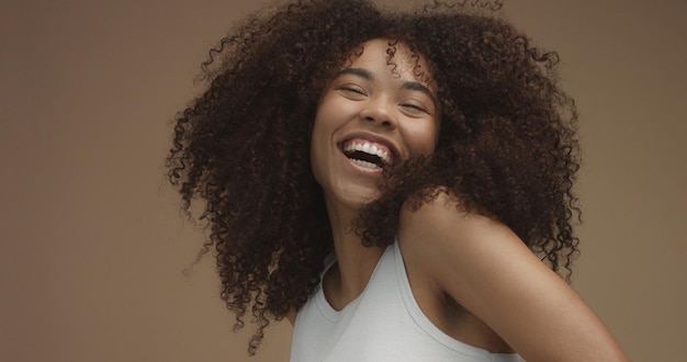Retrato de mujer negra de raza mixta con pelo rizado de pelo afro grande en fondo beige Risa natural