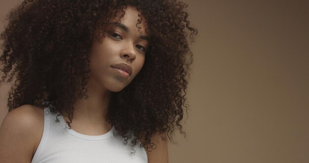 Retrato de mujer negra de raza mixta con pelo rizado de pelo afro grande en fondo beige