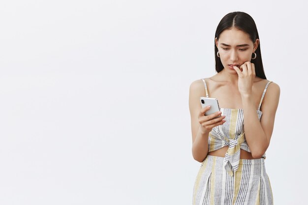 Retrato de mujer nerviosa intensa atractiva y elegante en traje lindo, mordiéndose las uñas mientras mira la pantalla del teléfono inteligente con ansiedad