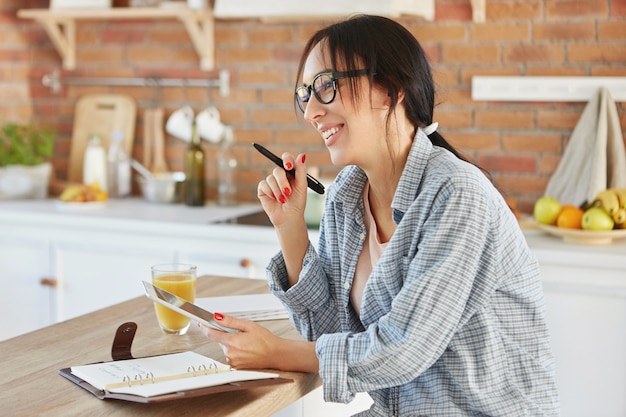 Retrato de mujer ocupada crea proyecto, busca información en tableta, escribe notas en el cuaderno