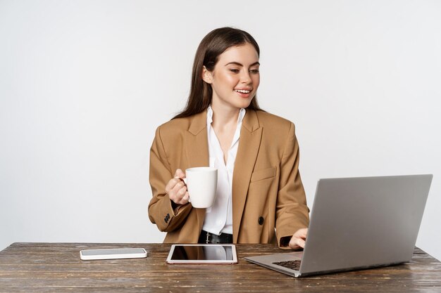 Retrato de mujer de oficina, empresaria directora ejecutiva que trabaja en una computadora portátil, bebe café y responde a los clientes en el sitio web, de pie sobre fondo blanco