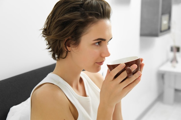 Foto gratuita retrato de una mujer oliendo café bebiendo la taza de la mañana en la cama despertando