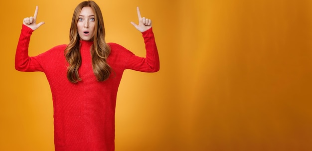 Retrato de mujer pelirroja atractiva y elegante en vestido rojo de punto jadeando de asombro abierto