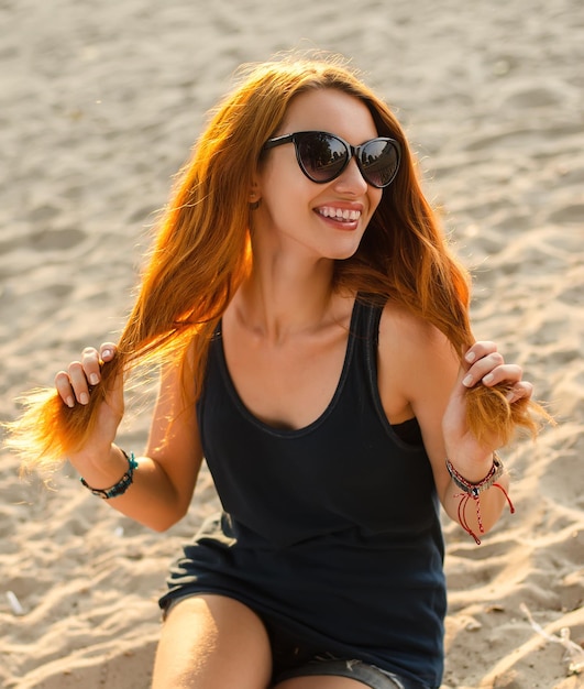 El retrato de una mujer pelirroja delgada se sienta en una playa.