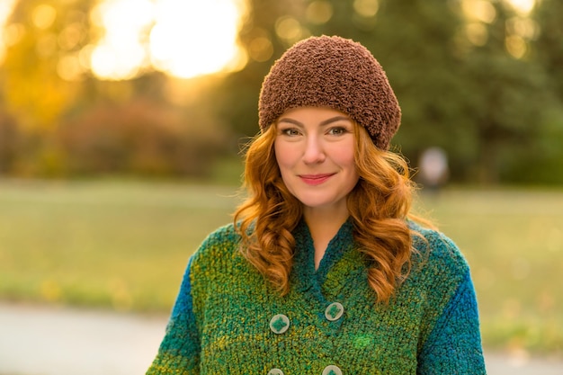 Retrato de mujer pelirroja emocionada sonriendo y posando para el fotógrafo Mujer hermosa feliz con sombrero marrón caminando en el parque de otoño