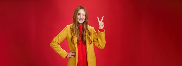 Retrato de mujer pelirroja feliz juguetona y linda con pecas en abrigo amarillo con la mano en la cintura