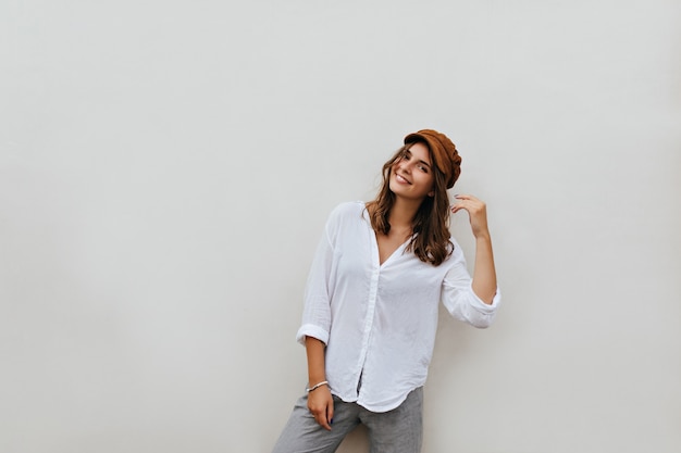 Foto gratuita retrato de mujer de pelo corto de ojos marrones con sombrero de terciopelo marrón, blusa de gran tamaño y pantalón gris en el espacio en blanco.