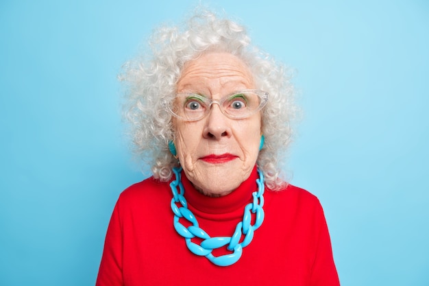 Retrato de mujer de pelo gris conmocionada mira con incredulidad