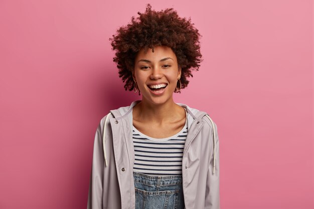 Retrato de mujer de pelo rizado sonríe felizmente a la cámara, se regocija en las próximas vacaciones