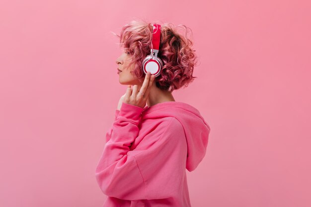 Retrato de mujer de pelo rosa rizado en enormes auriculares blancos
